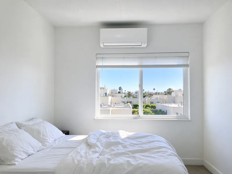 Condo bedroom with a white wall-mounted mini split head above a window looking over rooftops