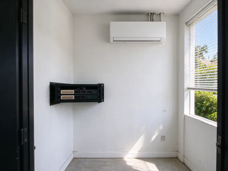 Network closet with a small equipment rack and a white mini split head high on the opposite wall