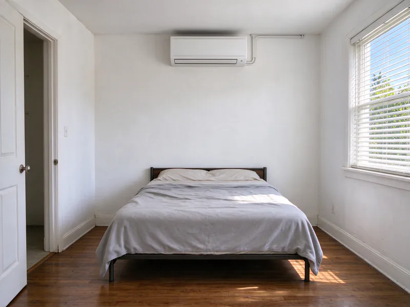 White wall-mounted mini split head installed high on the wall above a bed in a small San Diego bedroom
